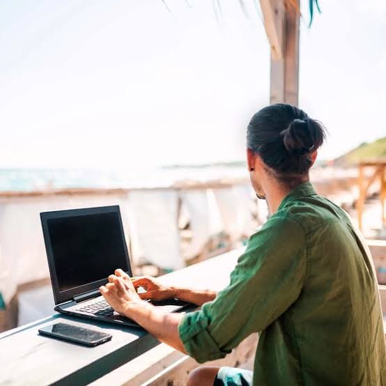 Una persona trabaja con su laptop tumbada en la arena de la playa