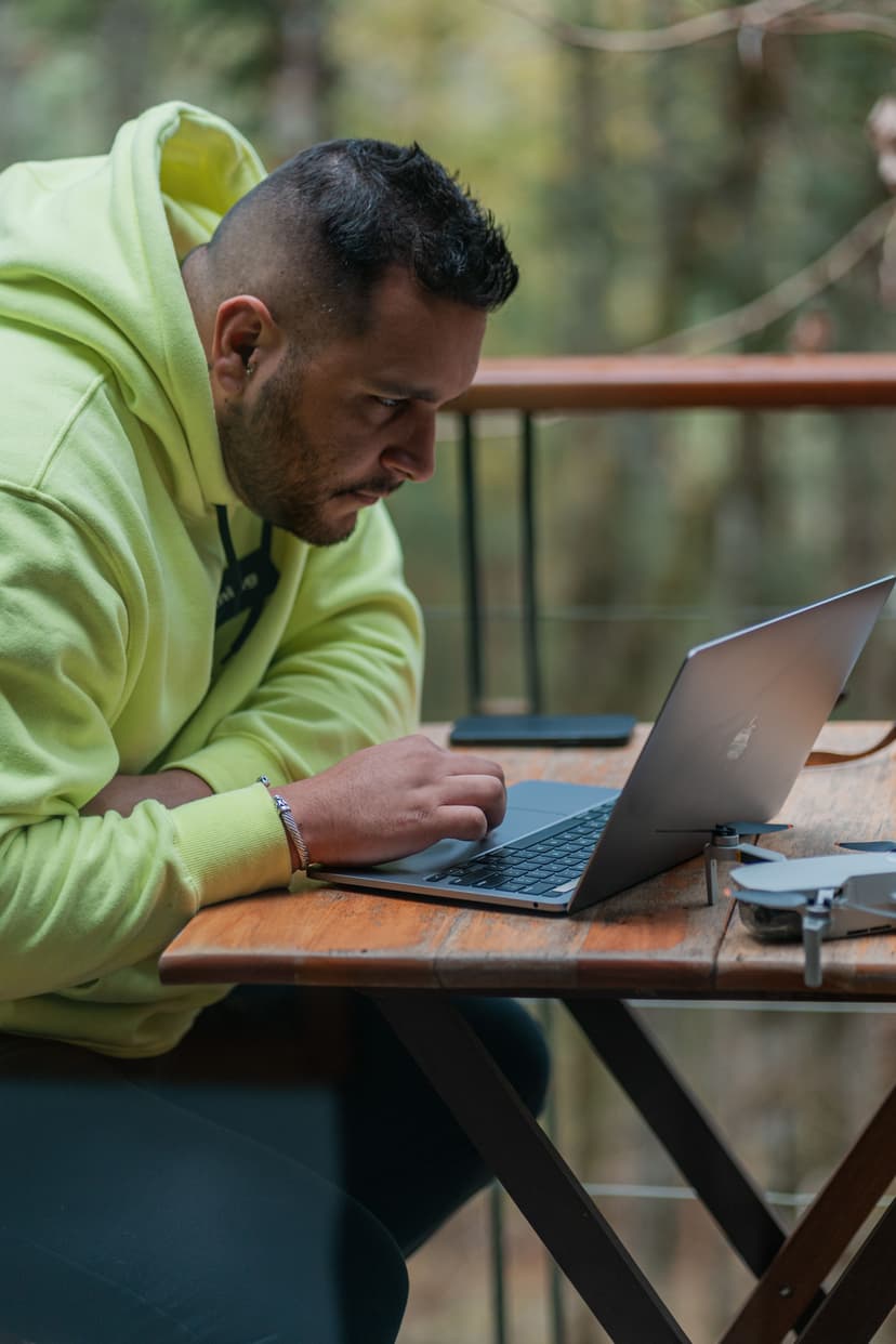 Un hombre trabaja concentrado en su laptop en una terraza de madera, con un dron sobre la mesa