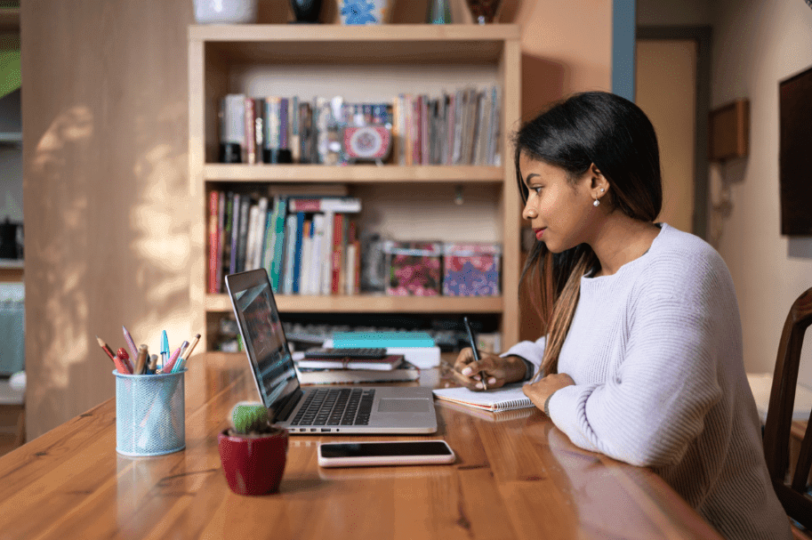 Una mujer estudia con su laptop y un cuaderno en la mesa de su casa
