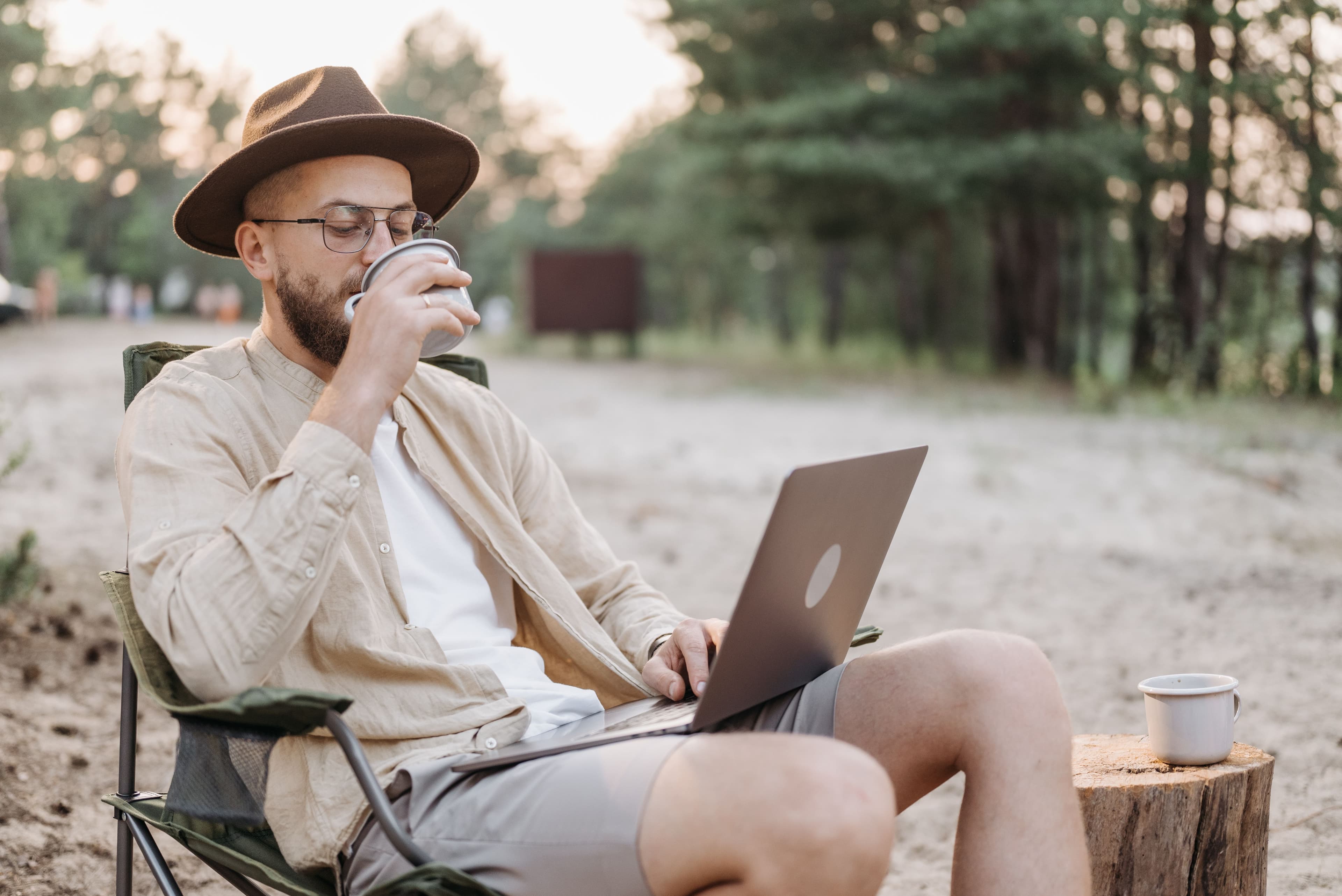Una persona toma café mientras trabaja con su computador al aire libre
