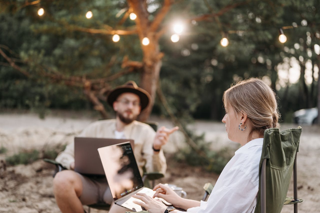 Two adults working on laptops in a rustic outdoor setting with ambient lighting.